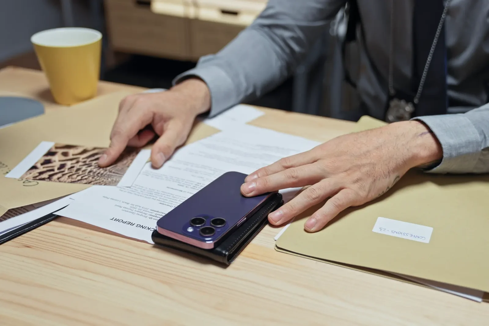 A person wearing reviews various documents, including a case report and a photograph of evidence, next to a smartphone on a desk.